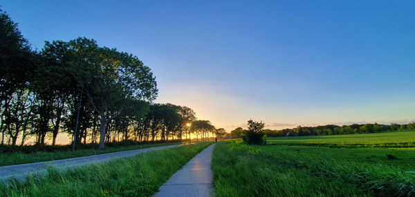 Empty road amidst field against sky during sunset
