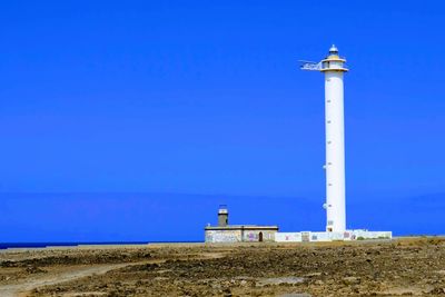 Lighthouse by building against clear blue sky