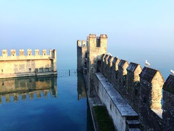 Seagull perching on fortified wall by river against clear sky