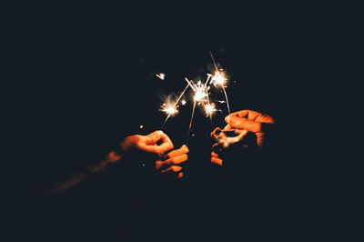 Close-up of friends holding illuminated sparklers at night