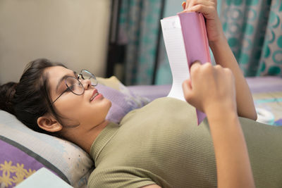 Young woman using mobile phone while lying on bed at home
