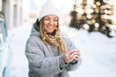 Blurred motion photo of young woman in warm clothes with sparkler near retro car in winter street