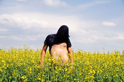 Man covering face with t-shirt while standing amidst flowering plants