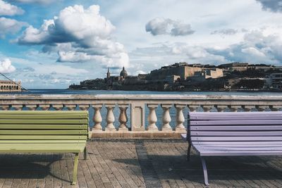 Empty benches on bridge against cloudy sky