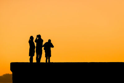 Silhouette men standing against orange sky