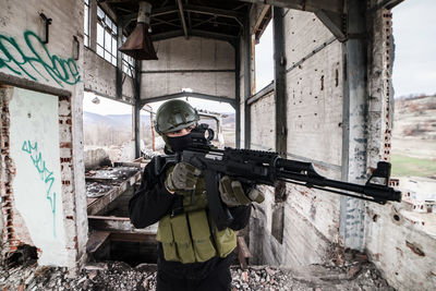 Sniper aiming rifle while standing outdoors