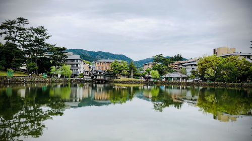 Reflection of trees and buildings in city against sky