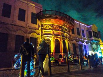 Rear view of people at illuminated building at night