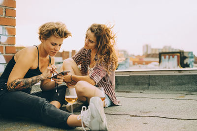 Woman showing mobile phone to friend while sitting on terrace during rooftop party