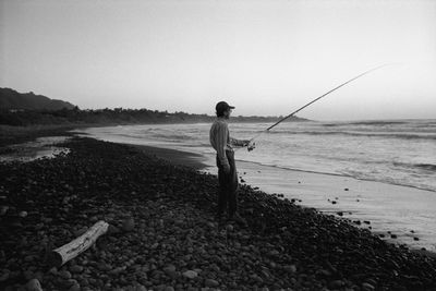 Rear view of man walking at beach against clear sky