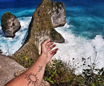 Cropped tattooed hand of person gesturing towards sea