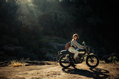 Full length of woman sitting on motorcycle against forest