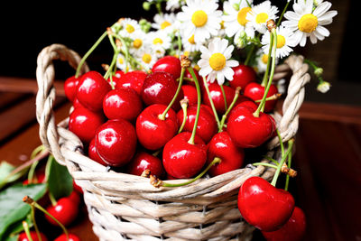 Basket with fruits and flowers on a wooden table close-up. ripe cherry with camomiles