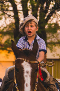 Thoughtful boy riding horse against tree