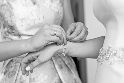 Midsection of bridesmaid assisting bride in wearing bracelet