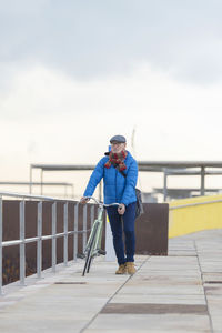 Man walking with bicycle on pier against sky