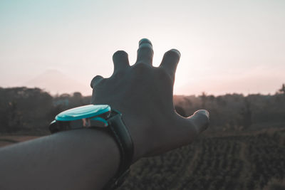 Cropped image of hand wearing wristwatch during sunset