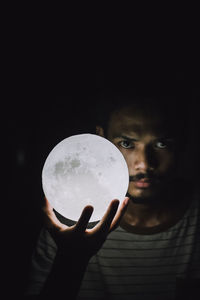 Close-up portrait of woman holding crystal ball against black background