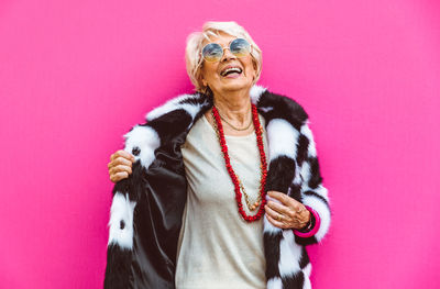 Portrait of smiling woman standing against pink background