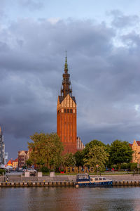 Clock tower amidst river and buildings against sky