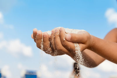 Cropped hands of boy playing with sand against blue sky