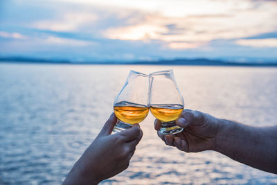 Close-up of hands toasting glasses against the lake