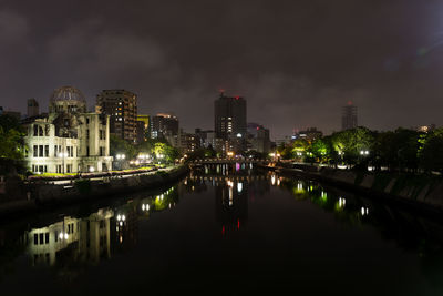 Illuminated buildings by river against sky in city at night