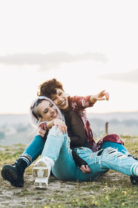 Full length of happy young woman sitting on land against sky