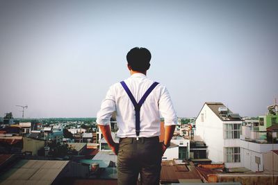 Rear view of man looking at cityscape against clear sky