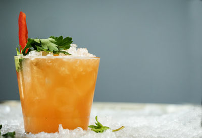 Close-up of drink garnish with bell pepper and herb in glass on crushed ice