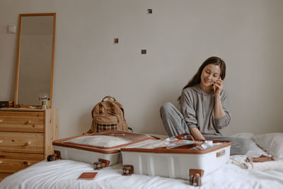 Woman calling friends before going to airport, open suitcase on the bed