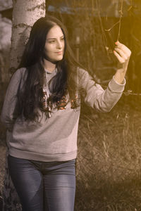 Young woman looking away while standing against tree