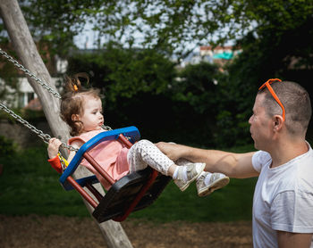 A man pushes a child on a swing in a park on a summer day.