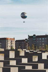 Hot air balloon flying over buildings in city against sky
