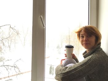 Portrait of woman holding coffee cup by window at home