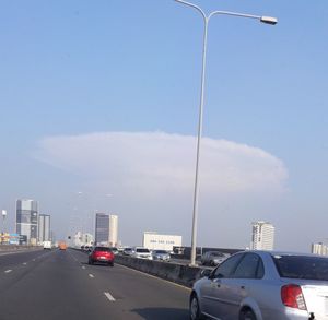 Cars on road by buildings against sky in city