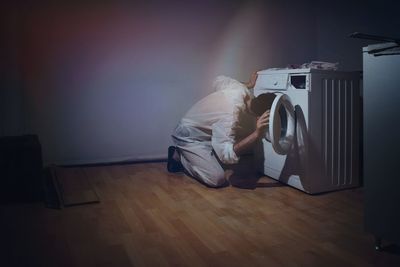 Young man looking in washing machine on hardwood floor at home