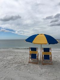 Deck chairs on beach against sky