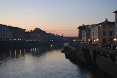 Bridge over river by buildings against sky at sunset