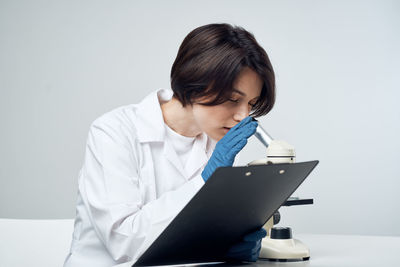 Young woman looking away while sitting on table against white background