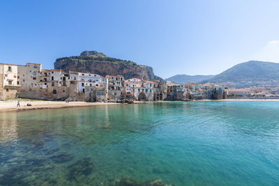 Scenic view of sea by buildings against clear blue sky