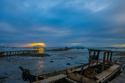 Old abandoned wooden boat at beach against cloudy sky at dusk