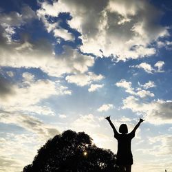 Low angle view of silhouette person standing by tree against sky