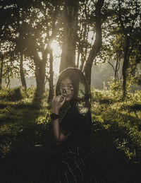 Portrait of young woman standing by trees in forest