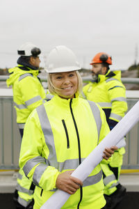 Engineers in reflective clothing standing on bridge with blueprints