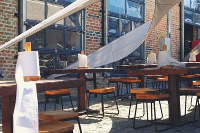 Empty chairs and tables at sidewalk cafe by building