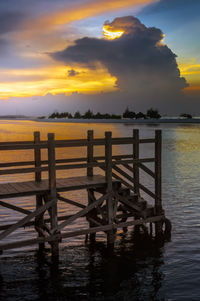 Wooden posts in sea against sky during sunset