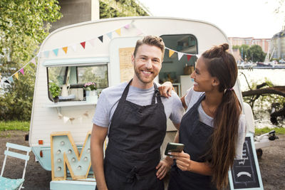 Portrait of happy owner standing with female colleague outside food truck on street