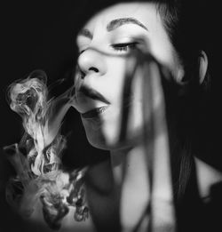 Close-up of young woman smoking against black background