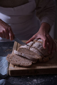 Hands slicing fresh bread, on dark background.